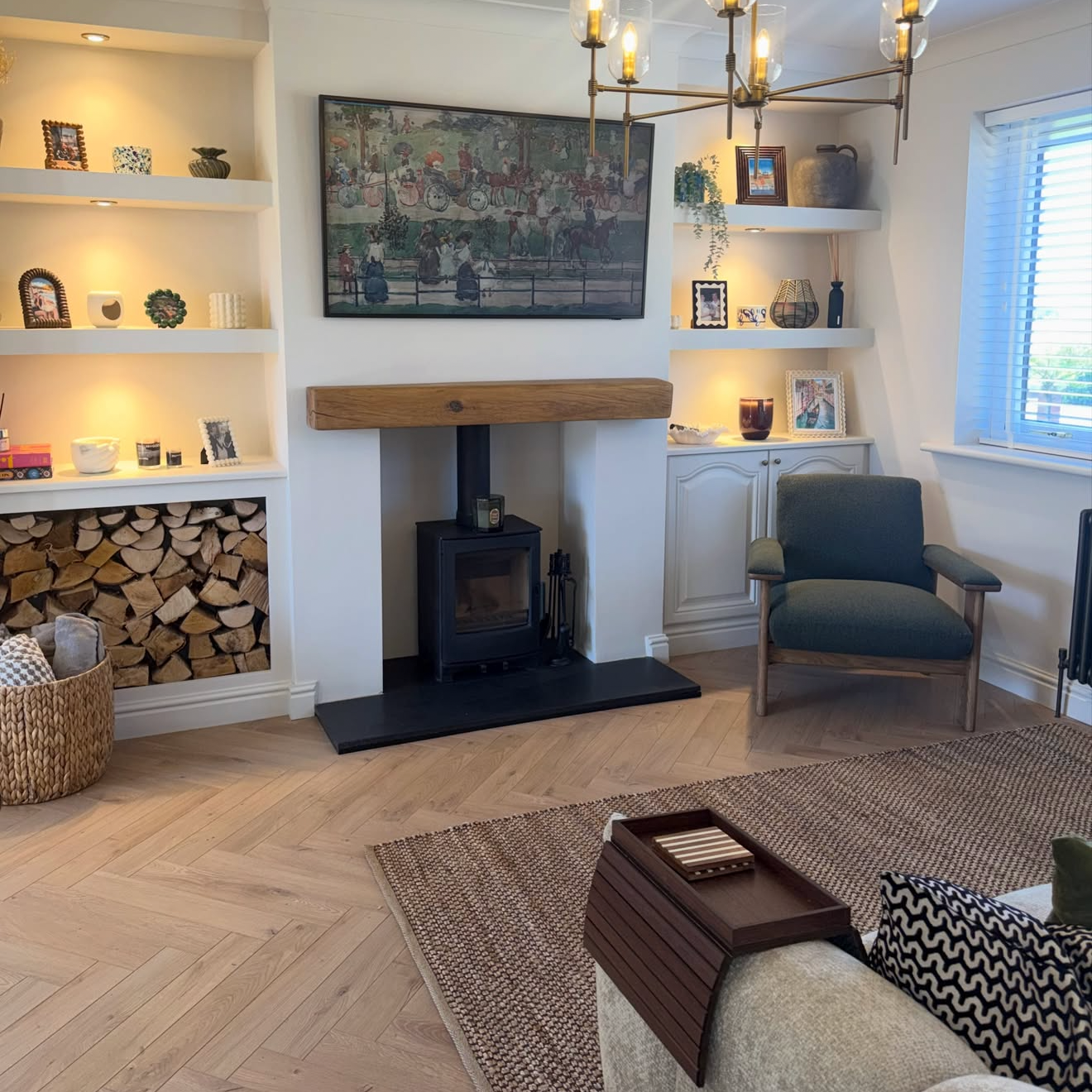 a cozy, modern living room interior with light wood floors, a fireplace, a chandelier, and a gray armchair.