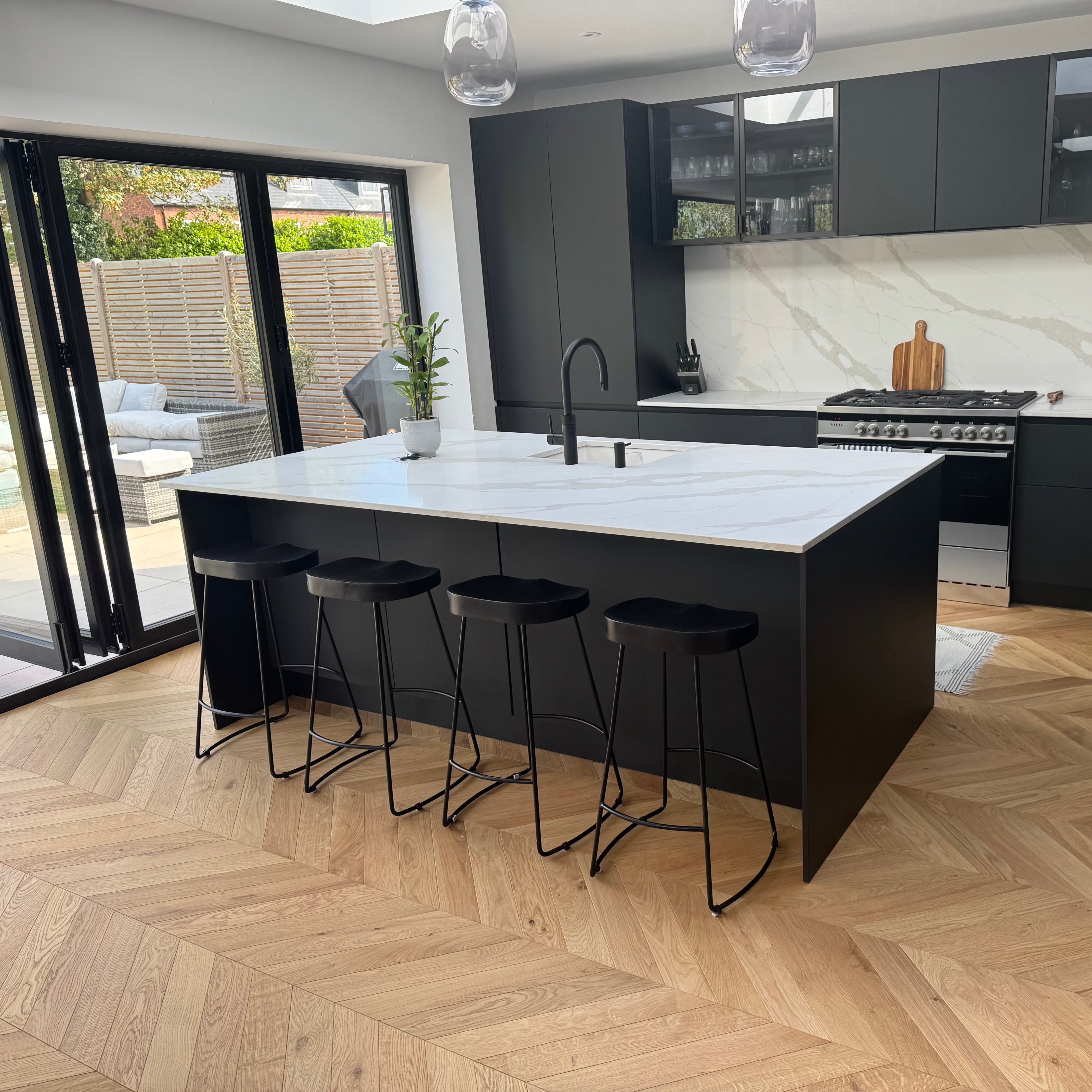 Modern kitchen with black island and bar stools on a wooden floor.