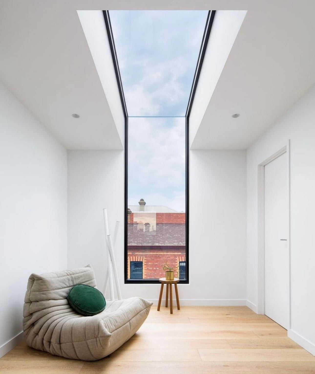 cream or grey togo sofa on wood floors in white room with large wall to ceiling windows and sky lights